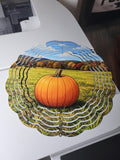 Wind spinner showing a bright orange pumpkin in a sunny autumn field with colorful fall foliage and blue sky