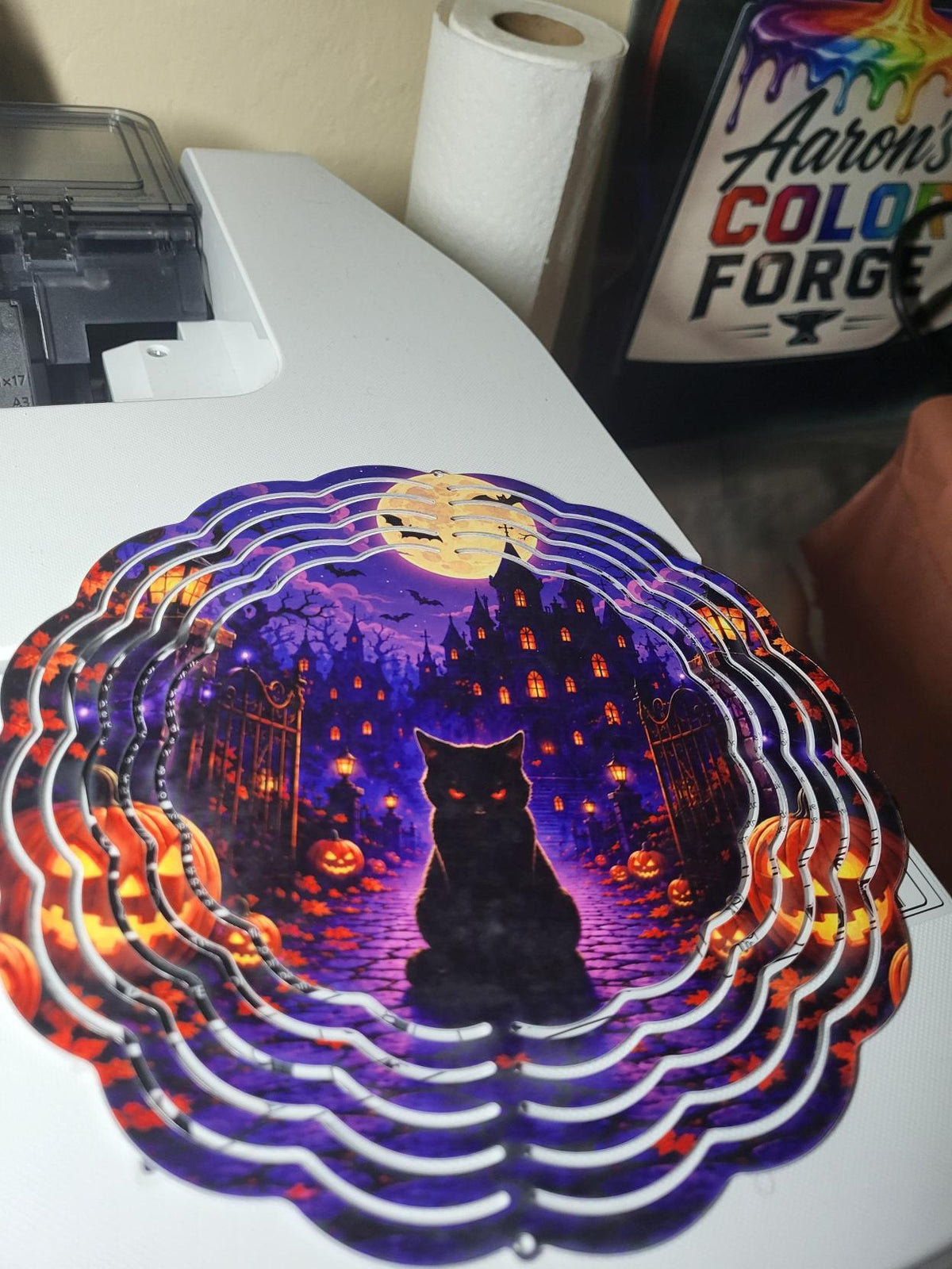 Halloween wind spinner featuring black cat with red glowing eyes on cobblestone path before haunted mansion with jack-o-lanterns and full moon