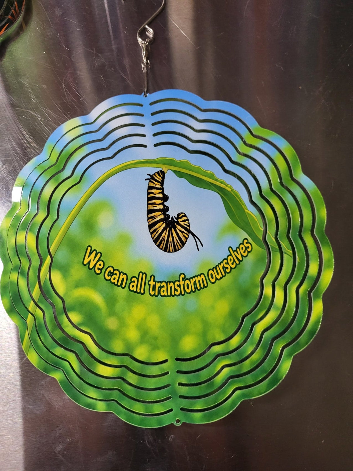 Wind spinner front side showing monarch caterpillar with quote We can all transform ourselves
